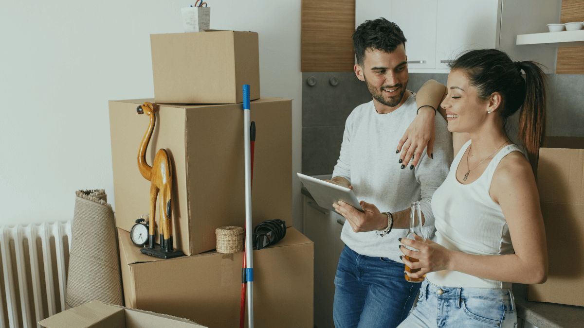 Couple using tablet to compare broadband providers while moving house with cardboard boxes in background