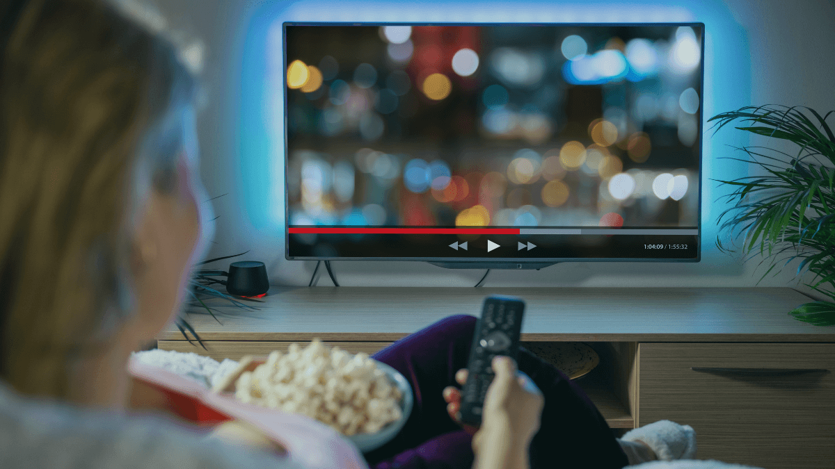 Person watching TV with smart speaker and remote showing bundled broadband and TV entertainment services